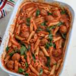 A white baking dish with dairy free baked penne and meatballs.