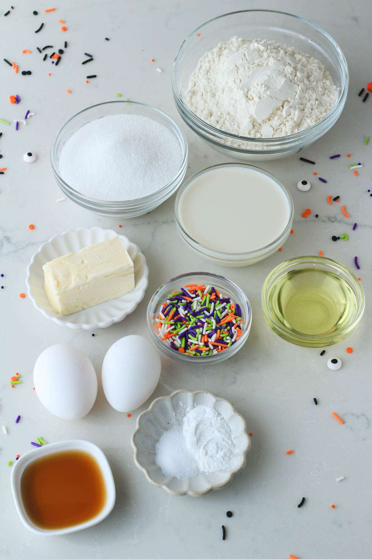 Ingredients for Halloween Funfetti Cupcakes on a white counter with sprinkles scattered around.