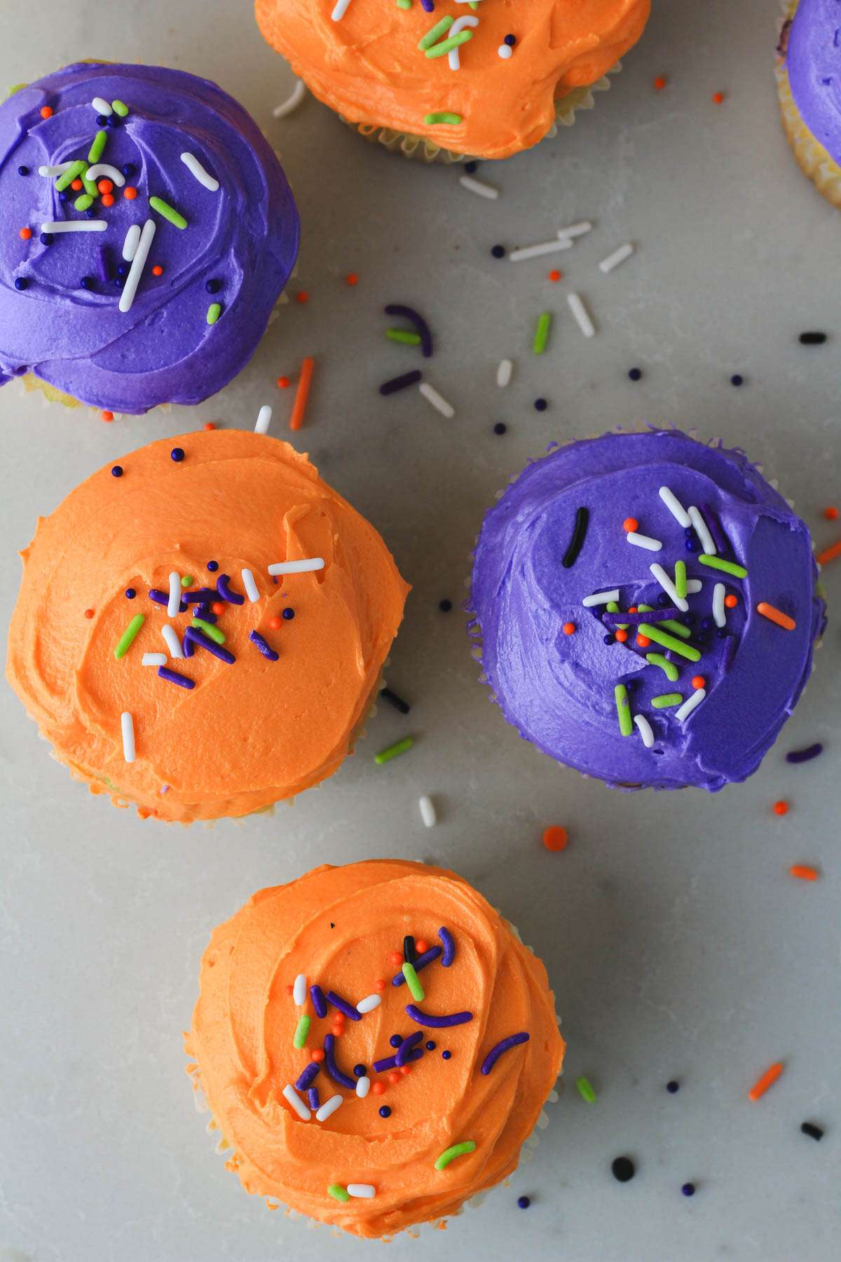 A top down picture of Halloween funfetti cupcakes topped with purple and orange icing on a white counter.