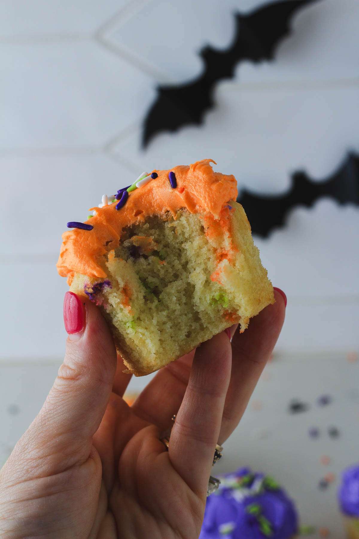 A hand holding a Halloween funfetti cupcake with a bite missing.