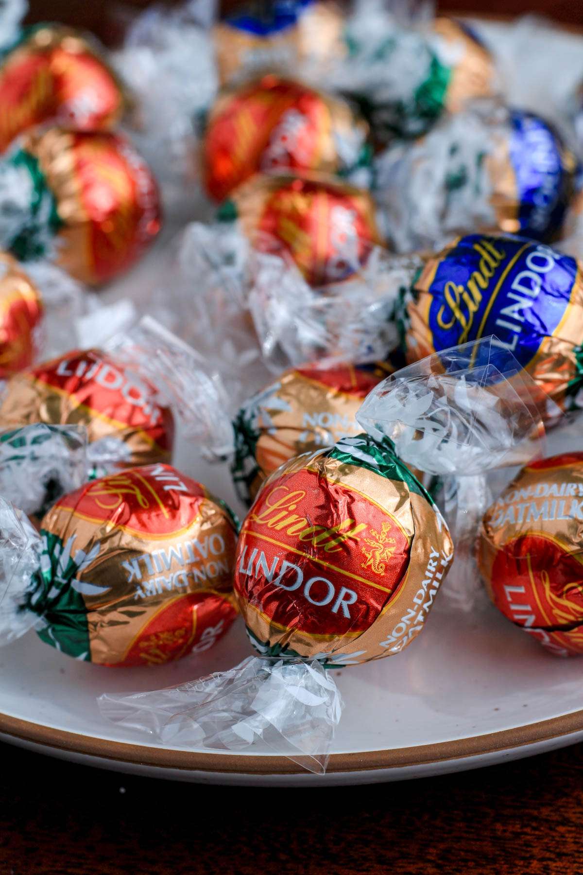 A white plate with a brown rim topped with red and blue wrapped non-dairy Lindt chocolate truffles.