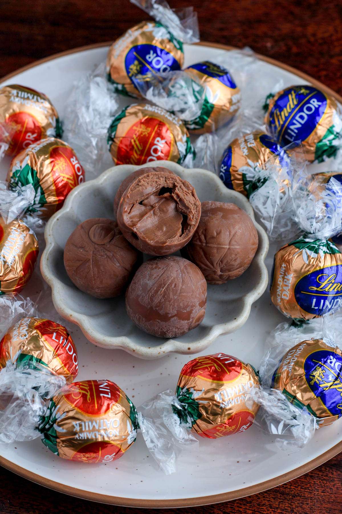 A white plate with a smaller plate on top with unwrapped chocolate truffles surrounded by wrapped chocolate truffles.