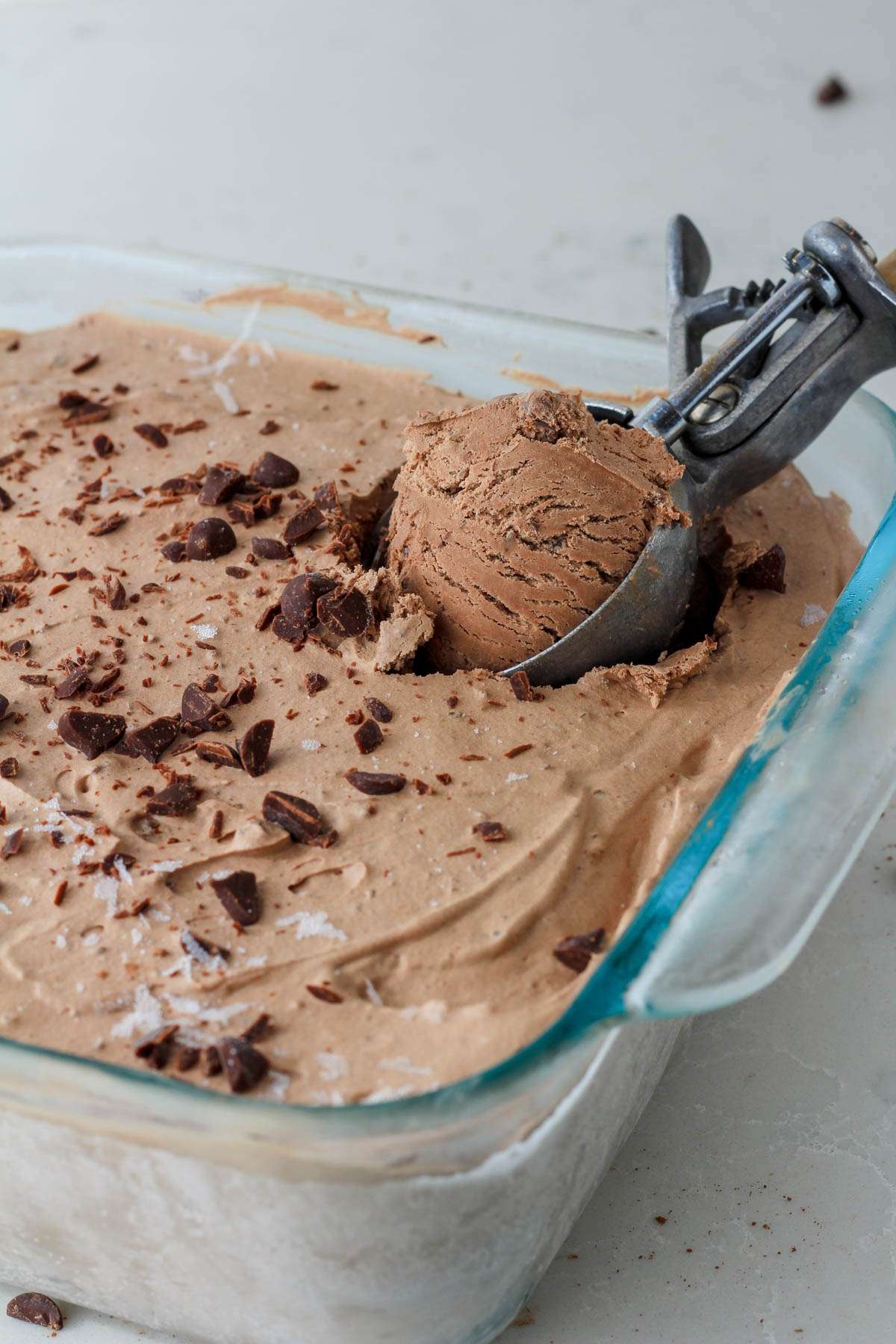 An ice cream scoop in a glass pan scooping out vegan chocolate ice cream with chocolate chips.