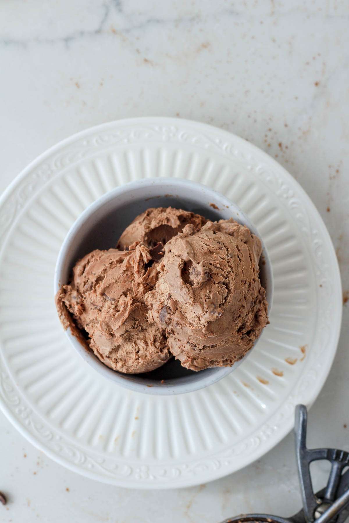 A white plate with a white bowl filled with vegan no churn chocolate chocolate chip ice cream.