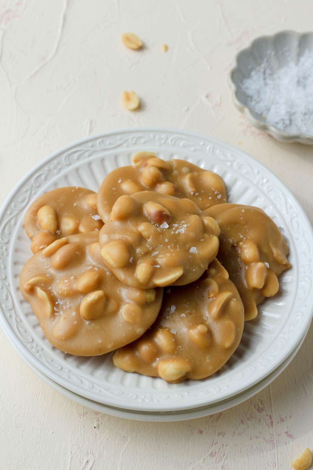 A plate with peanut pralines in front of a small pinch bowl of salt in the back right.