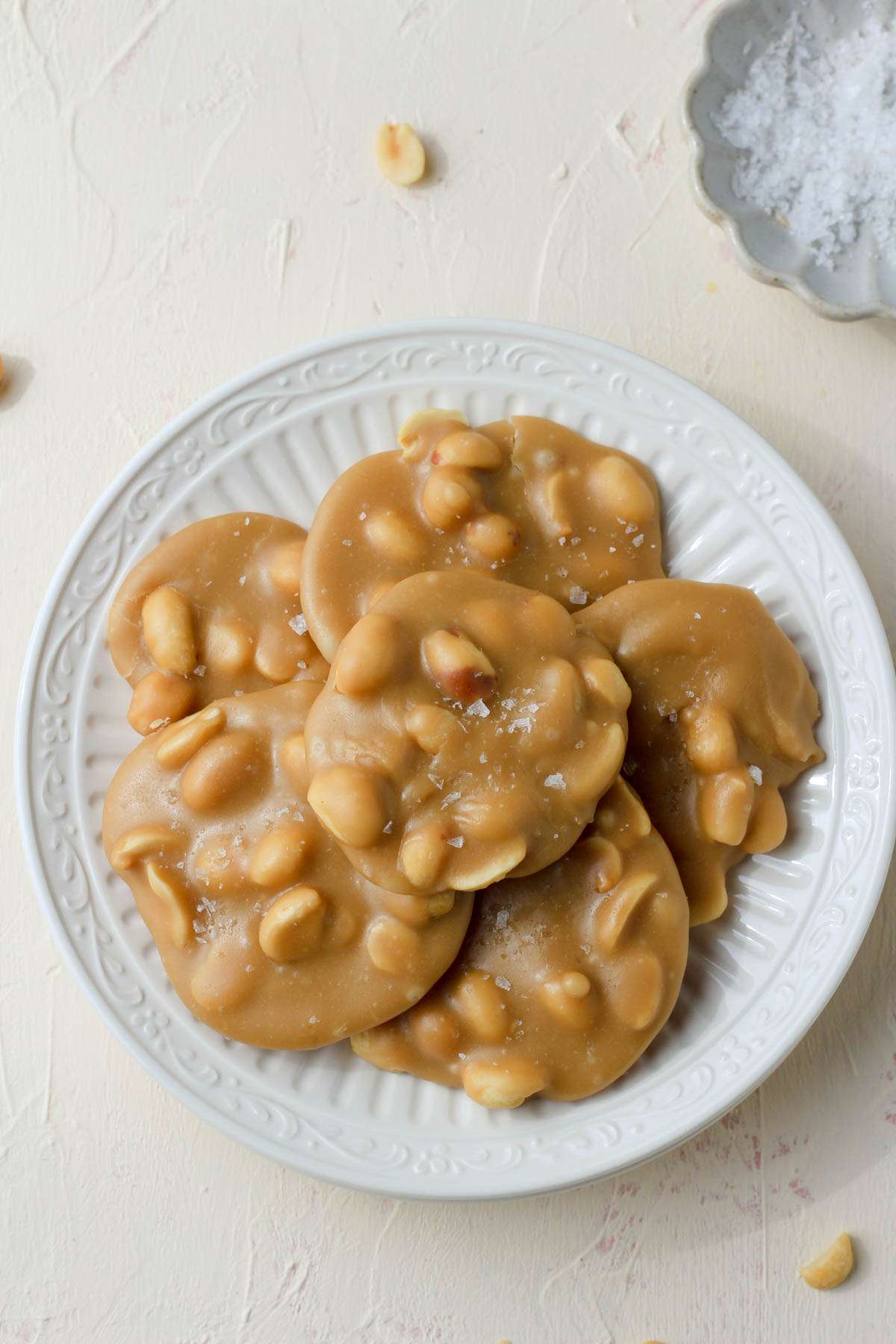 A top down photo of peanut pralines on a white plate with a small pinch bowl of salt in the top right.