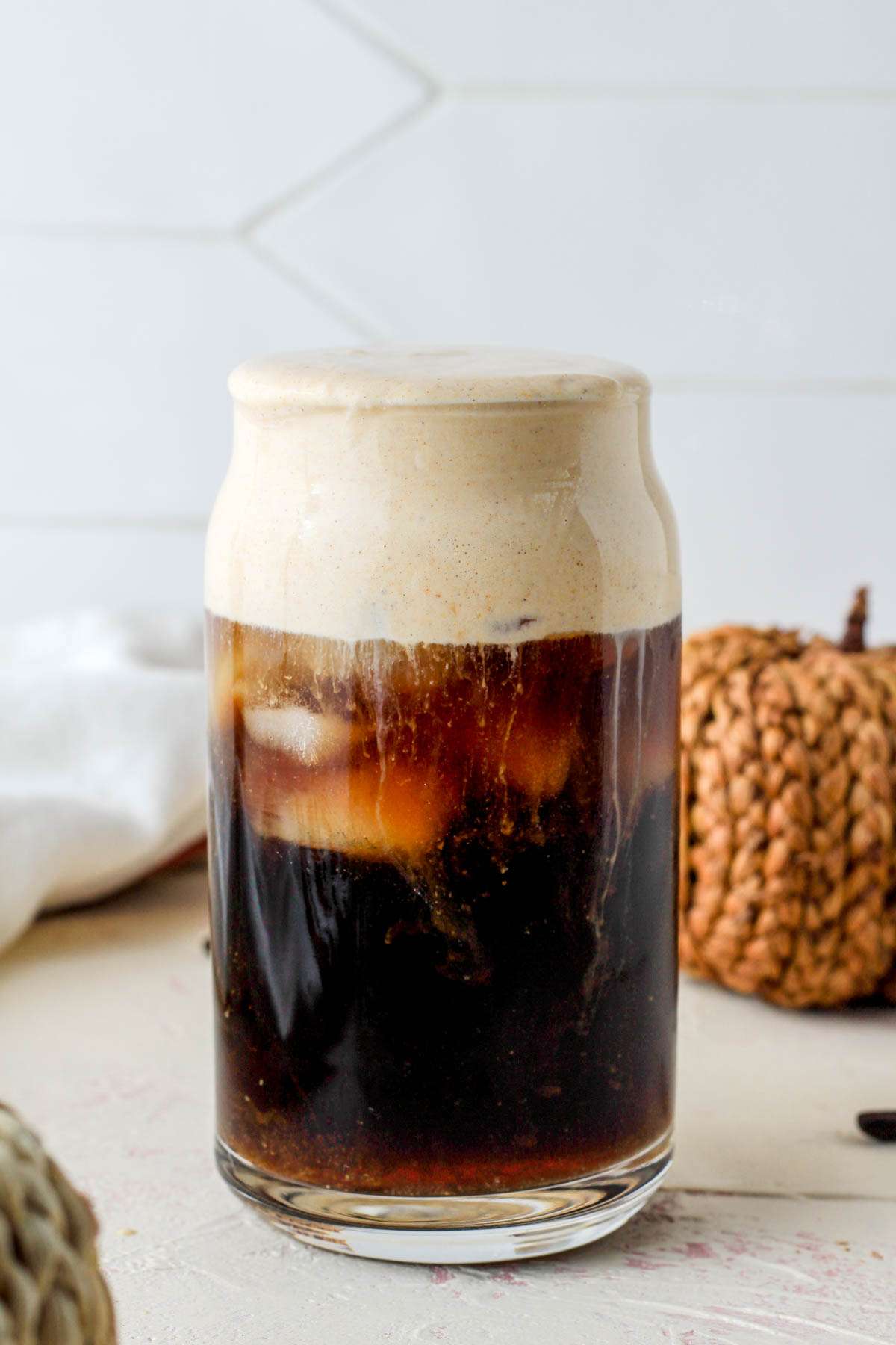 A glass of iced coffee topped with vegan pumpkin cream cold foam.