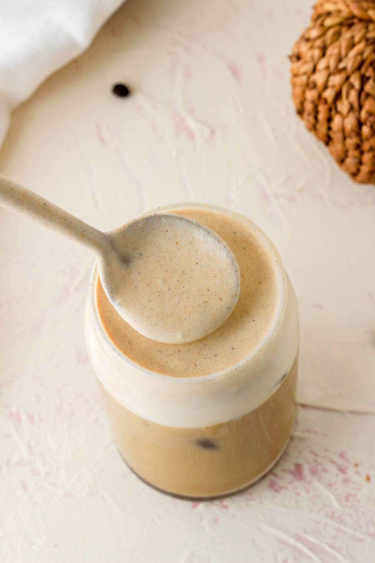 A spoon scooping the pumpkin spice cold foam out of the top of the iced coffee cup.