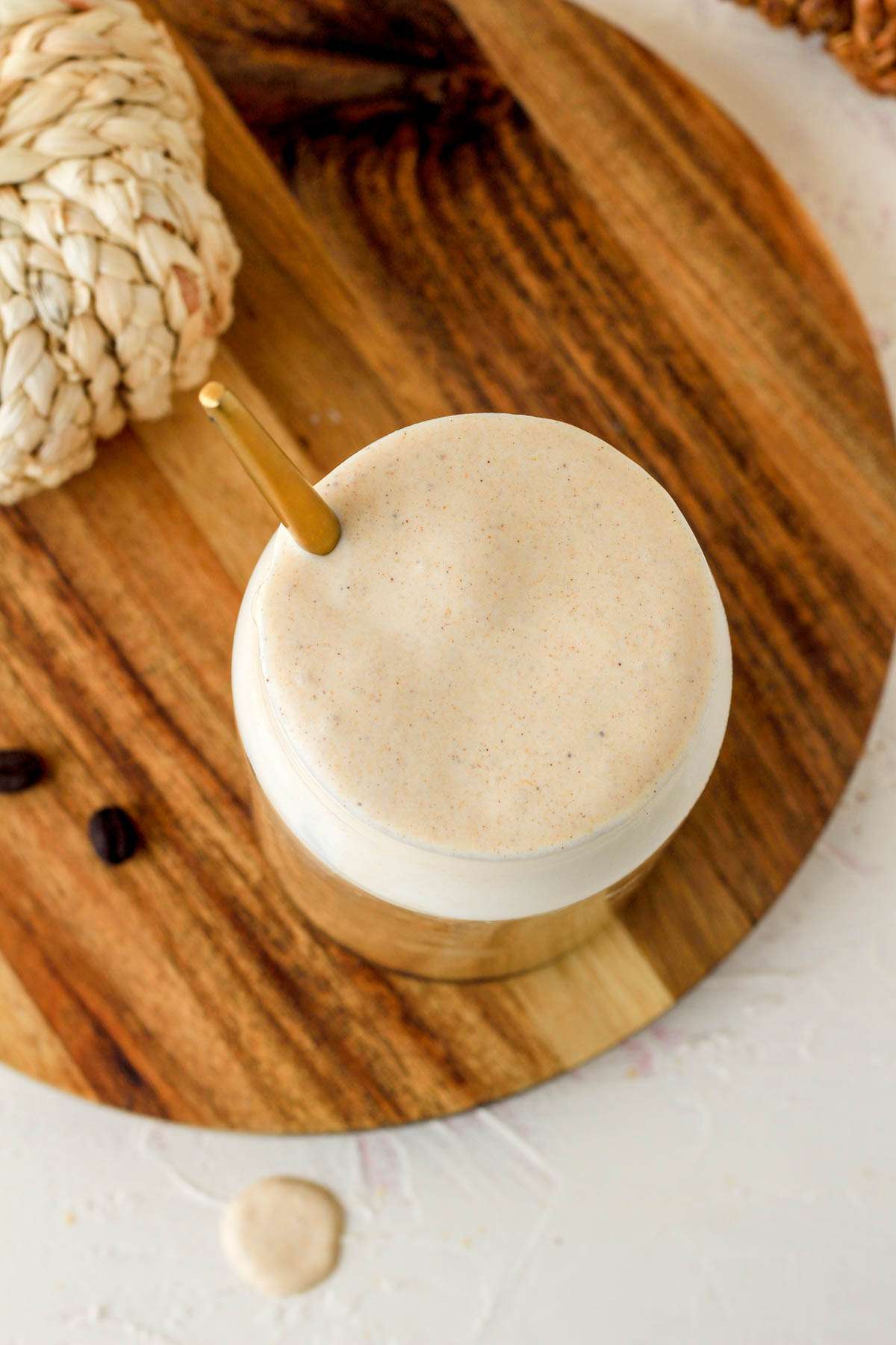 A top down of a glass of pumpkin spice cold foam topped coffee with a gold spoon in the left of the glass.