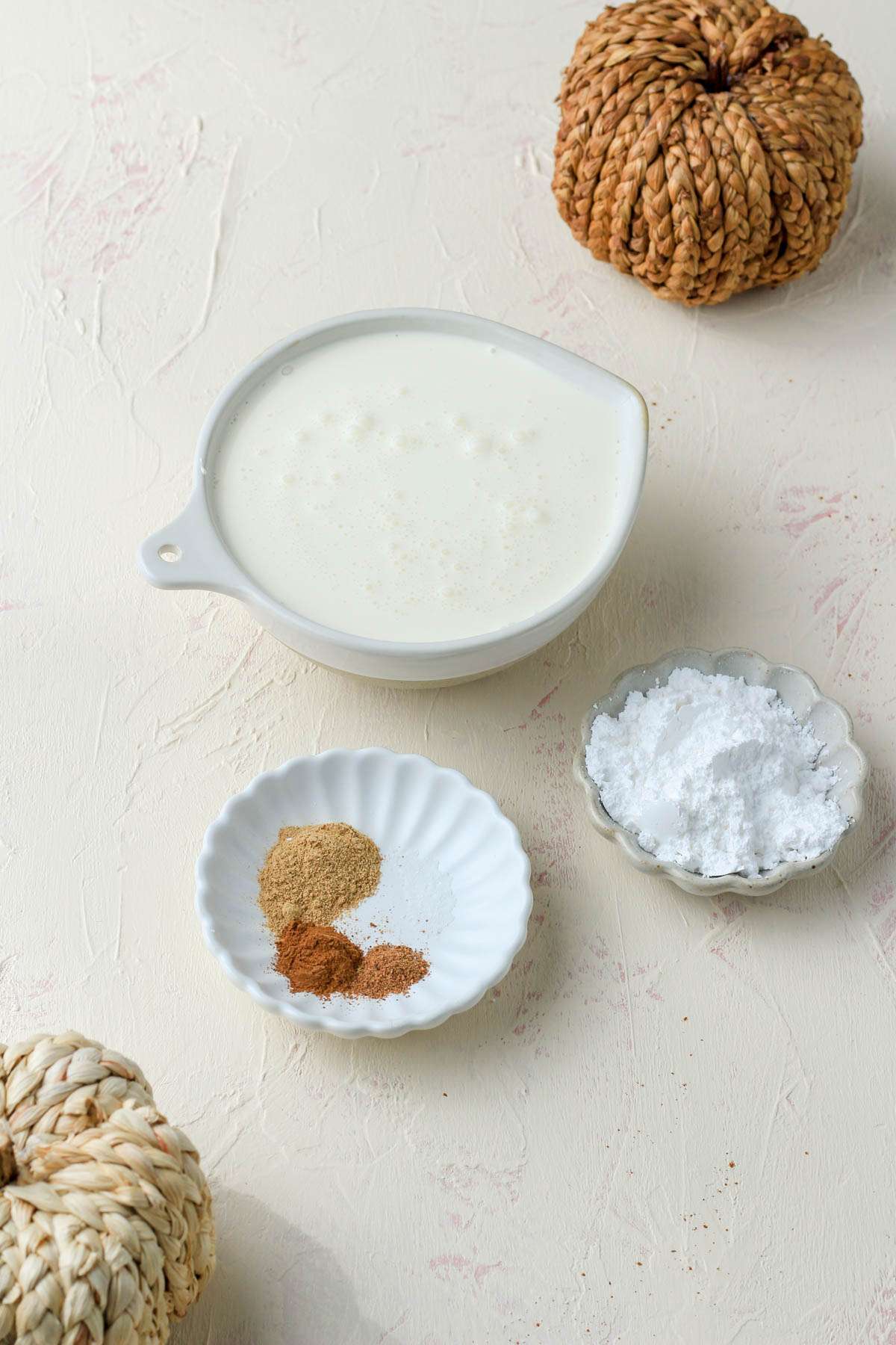 Ingredients for vegan pumpkin spice whipped cream on a cream counter with woven pumpkins.