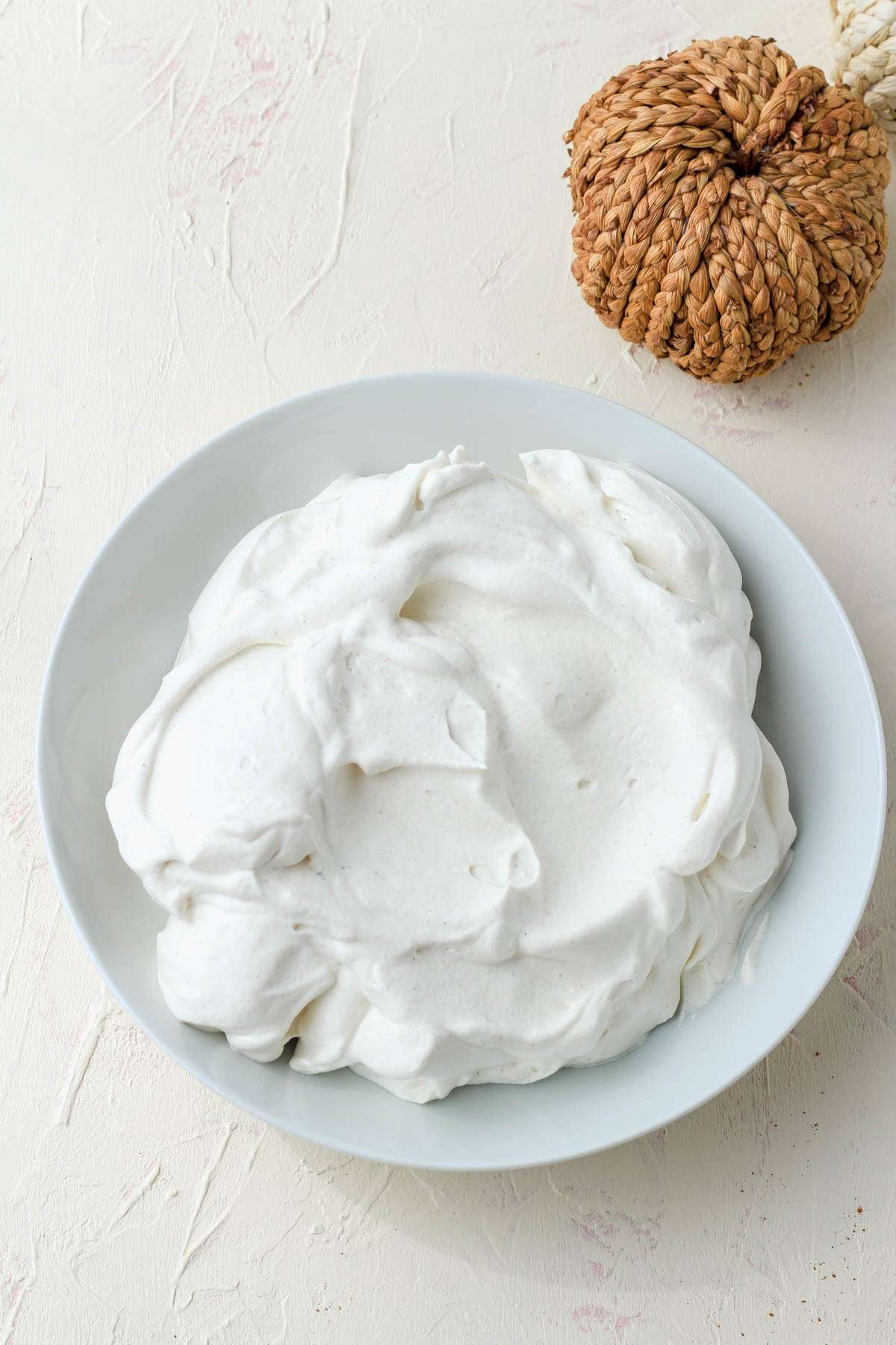 A white bowl with pumpkin spice whipped cream and an orange pumpkin in the top left.