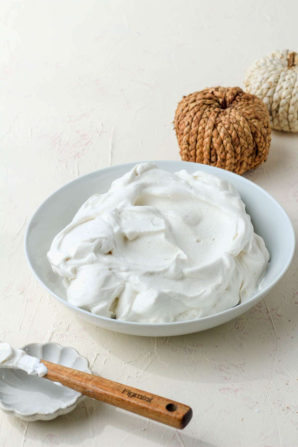 A white bowl of pumpkin spice flavored whipped cream on a cream counter with a spatula in the front left.