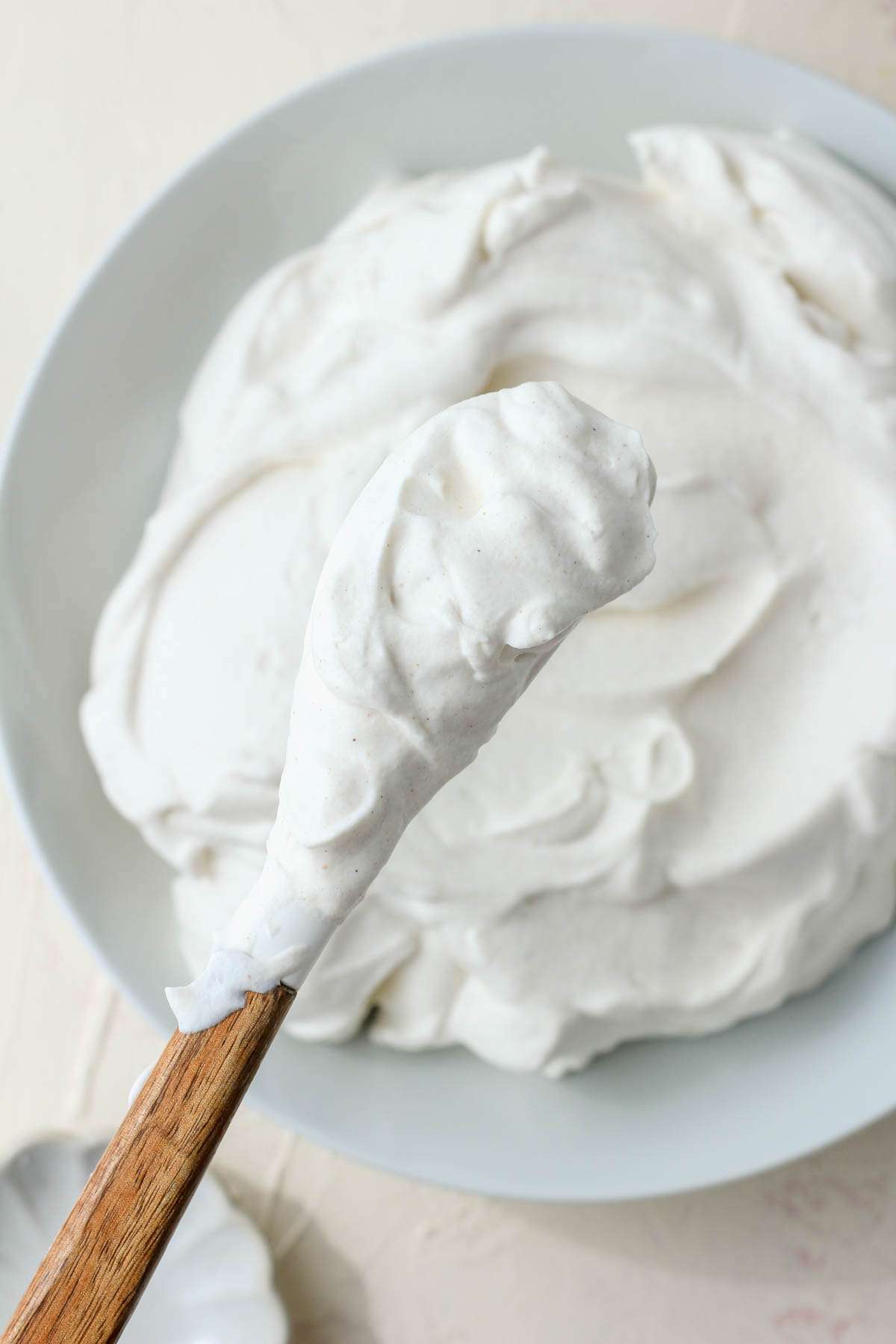 A spatula with a wooden handle and a scoop of vegan whipped cream over a white bowl of pumpkin spice whipped cream.
