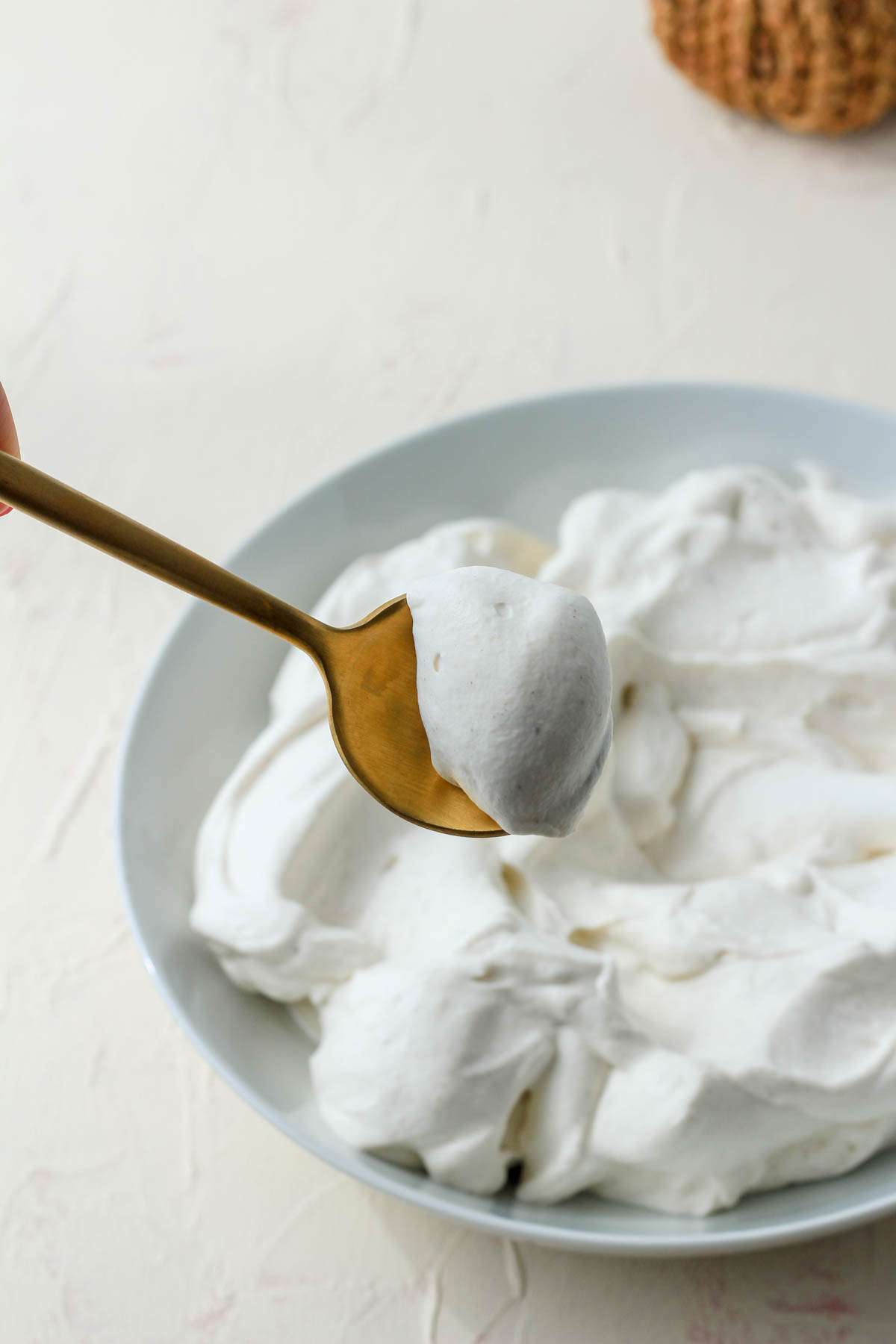 A gold spoon with a scoop of vegan pumpkin spice whipped cream in front of a white bowl of vegan whipped cream.