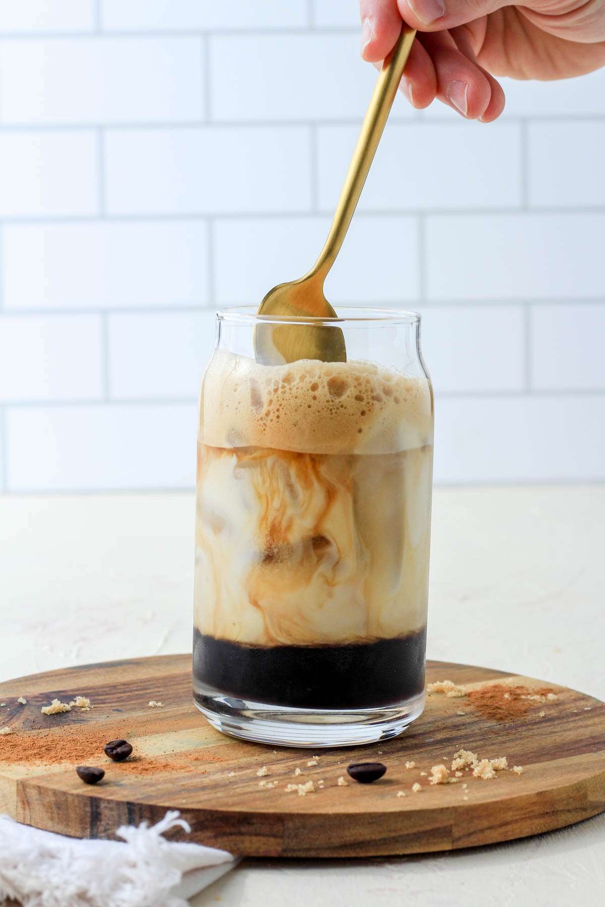 A gold spoon at the top of the brown sugar oat milk shaken espresso before mixing the oat milk into the coffee.