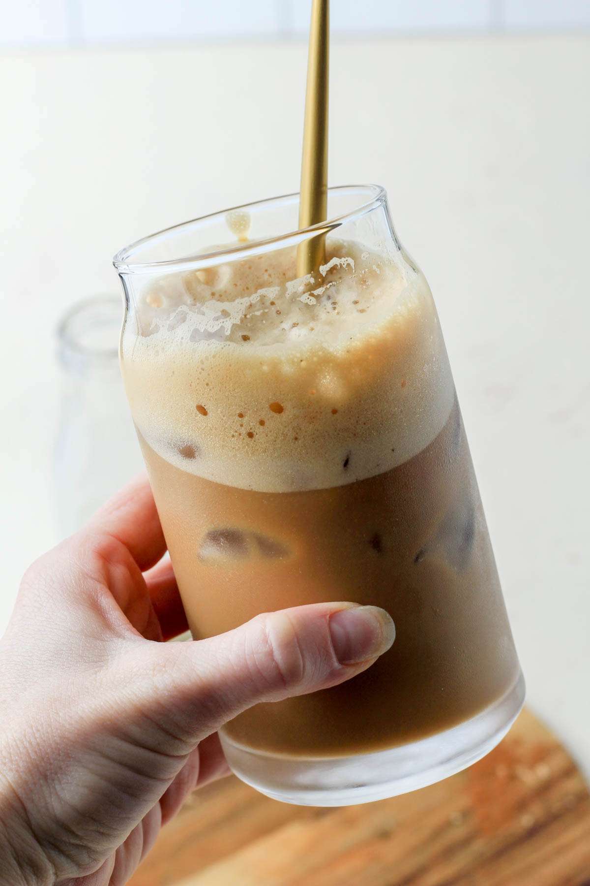 A hand holding a glass cup with a vegan brown sugar oat milk shaken espresso with a gold spoon poking out of the top.