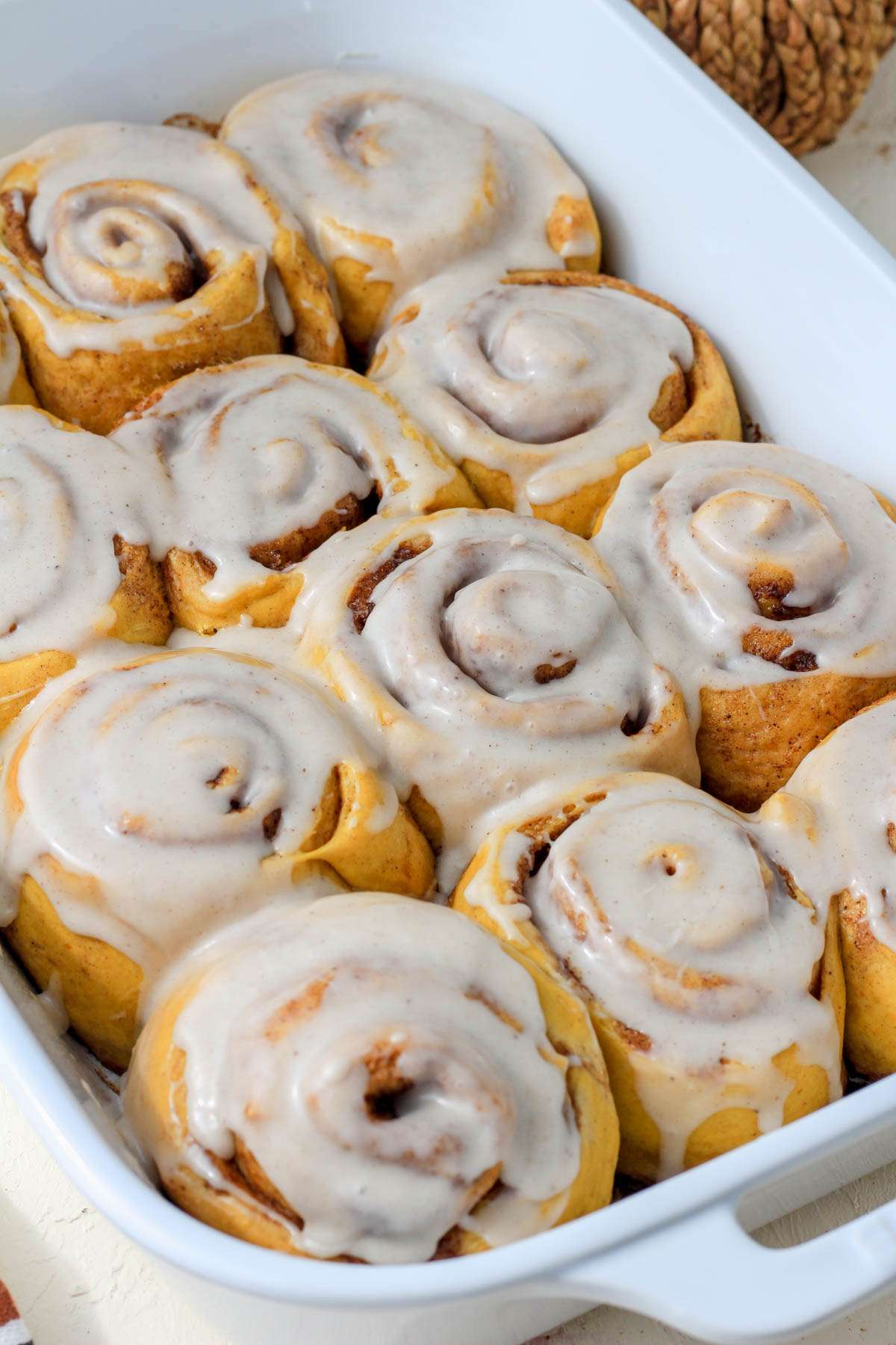 A white baking dish with dairy-free pumpkin spice cinnamon rolls topped with dairy-free icing.