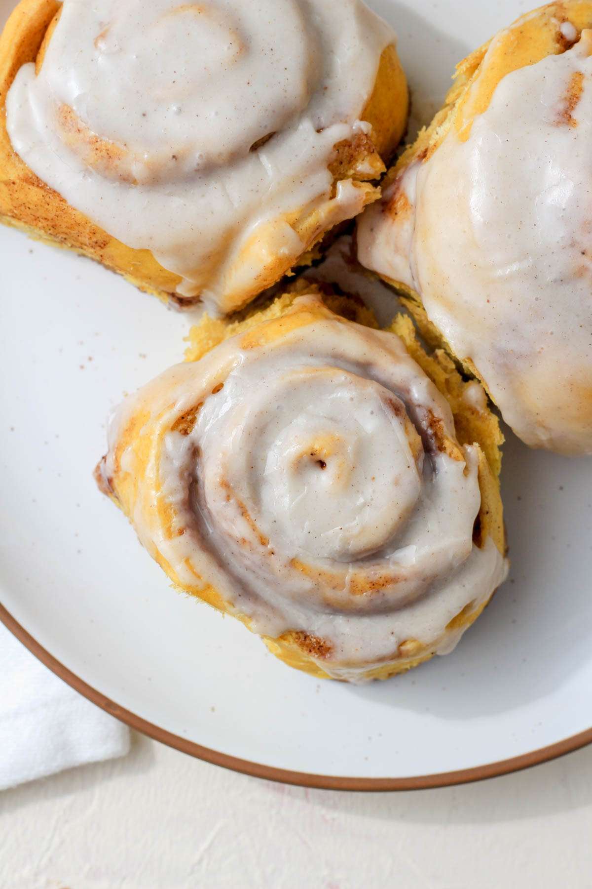 A white plate with a brown rim topped with three pumpkin spice cinnamon rolls.
