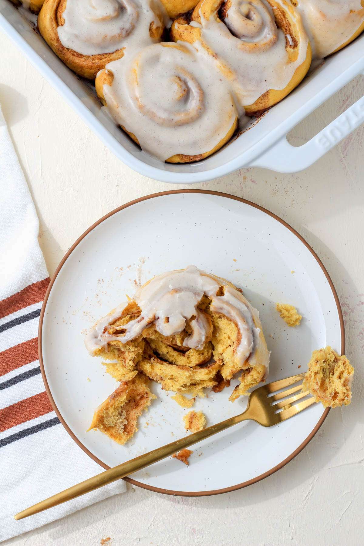 A white plate with a brown rim and a dairy-free pumpkin spice cinnamon roll with a gold fork.