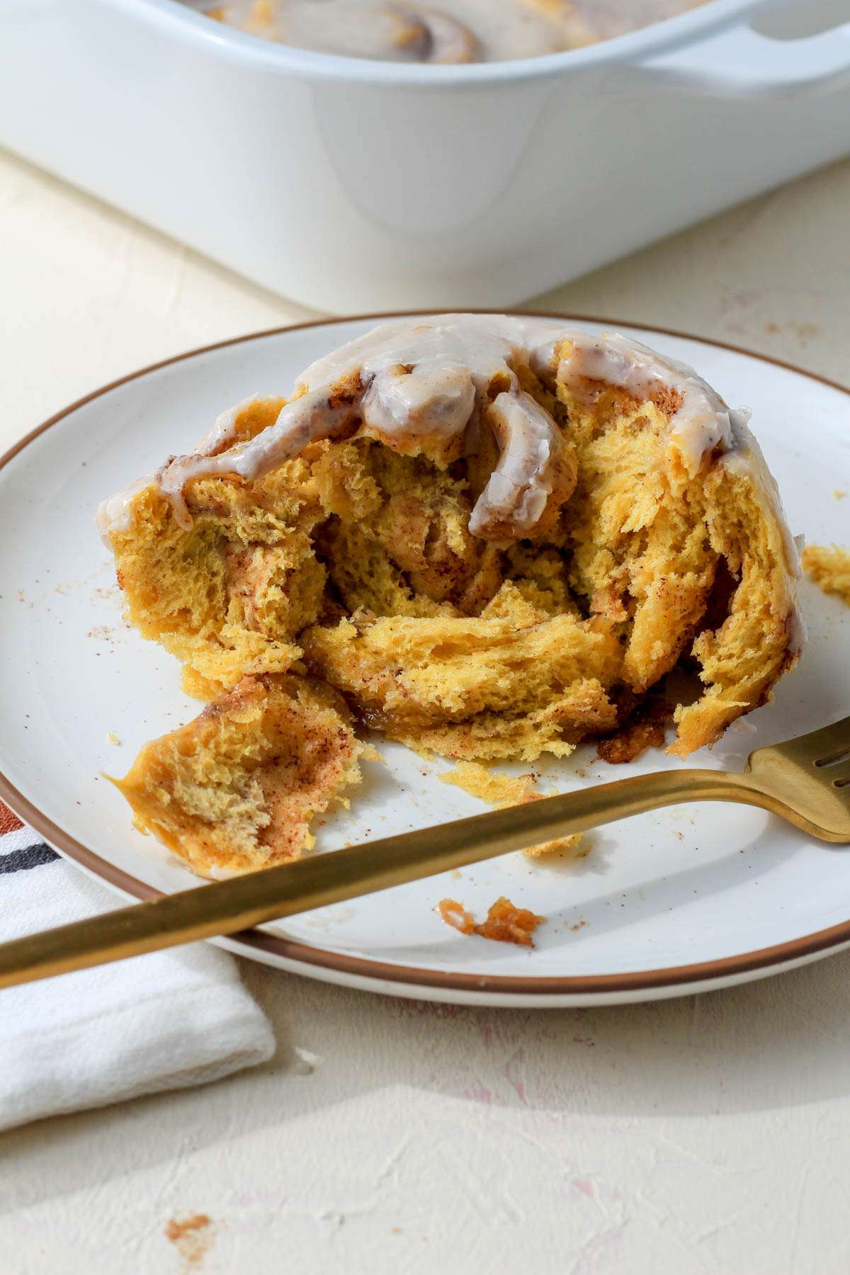 A broken apart dairy-free pumpkin spice cinnamon roll with a gold fork in front.