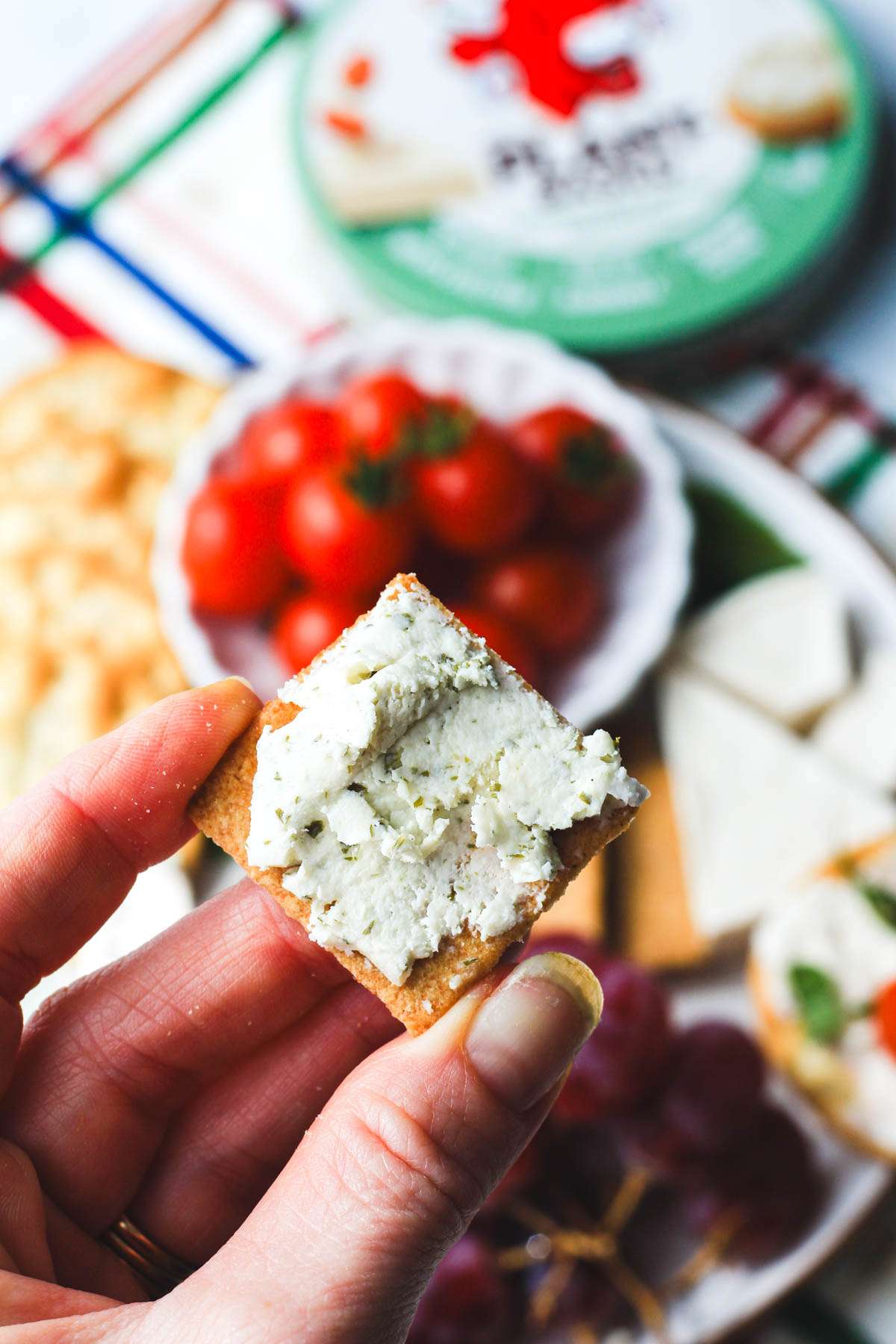 A square cracker topped with garlic and herb plant-based spreadable cheese.