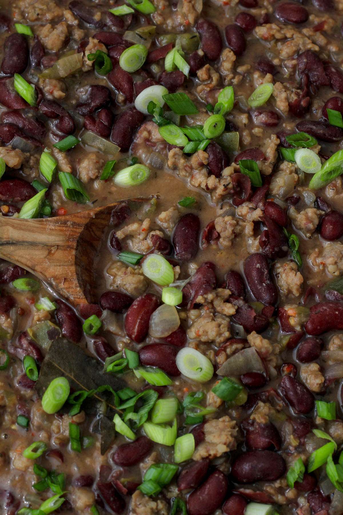 A close up of a wooden spoon with the sausage and red beans mixture topped with green onion.