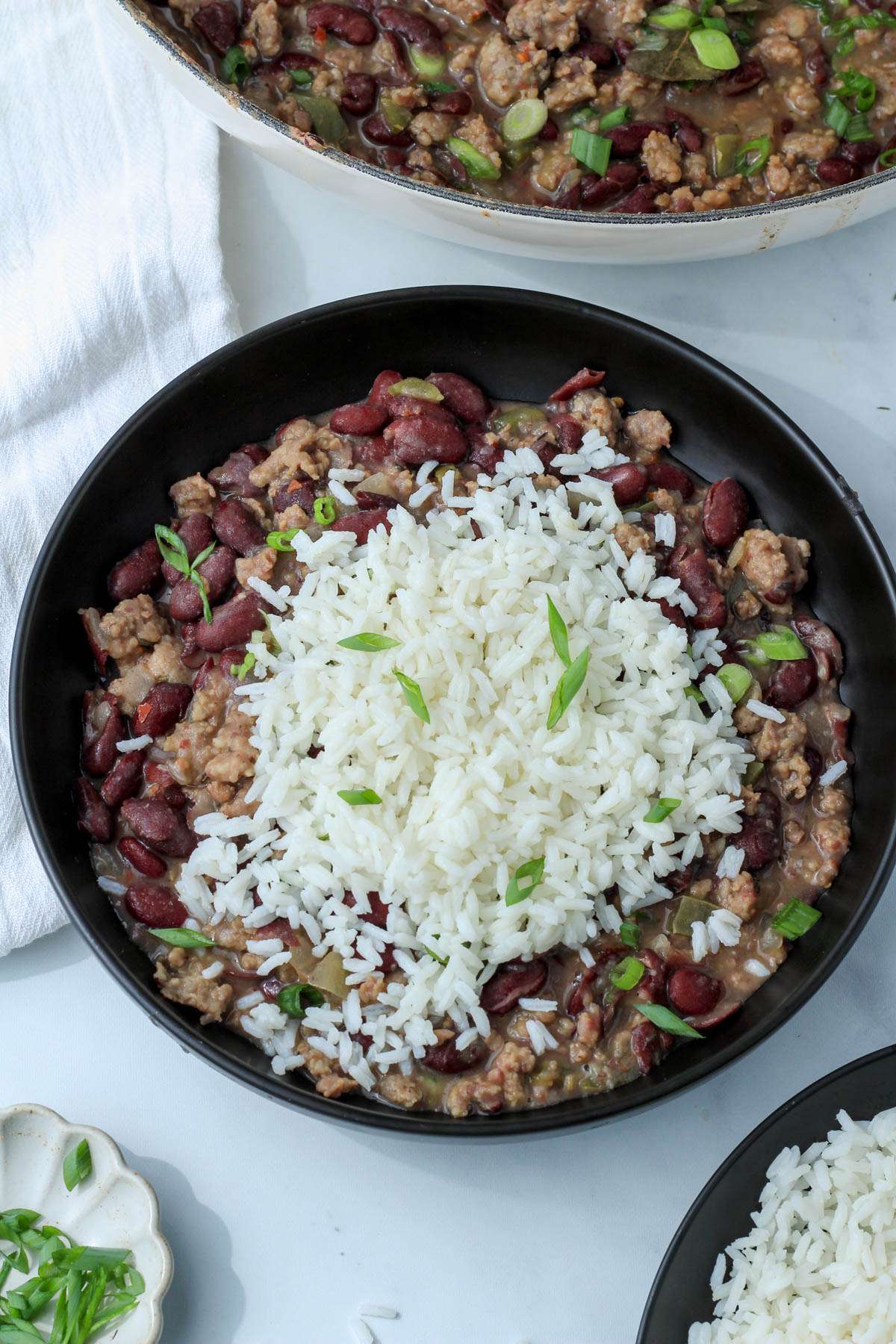A serving of red beans and rice in a black bowl topped with green onion.