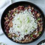 A close up of a black bowl with red beans and rice topped with chopped green onion.