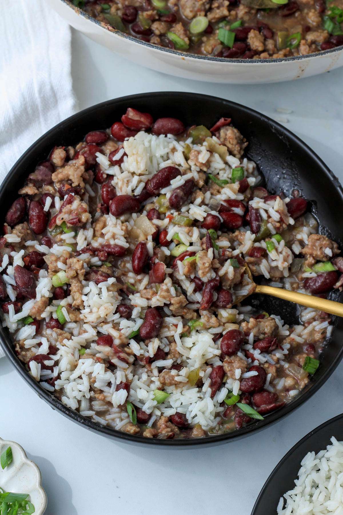 A black bowl with a gold spoon and a stirred up serving of red beans and rice.