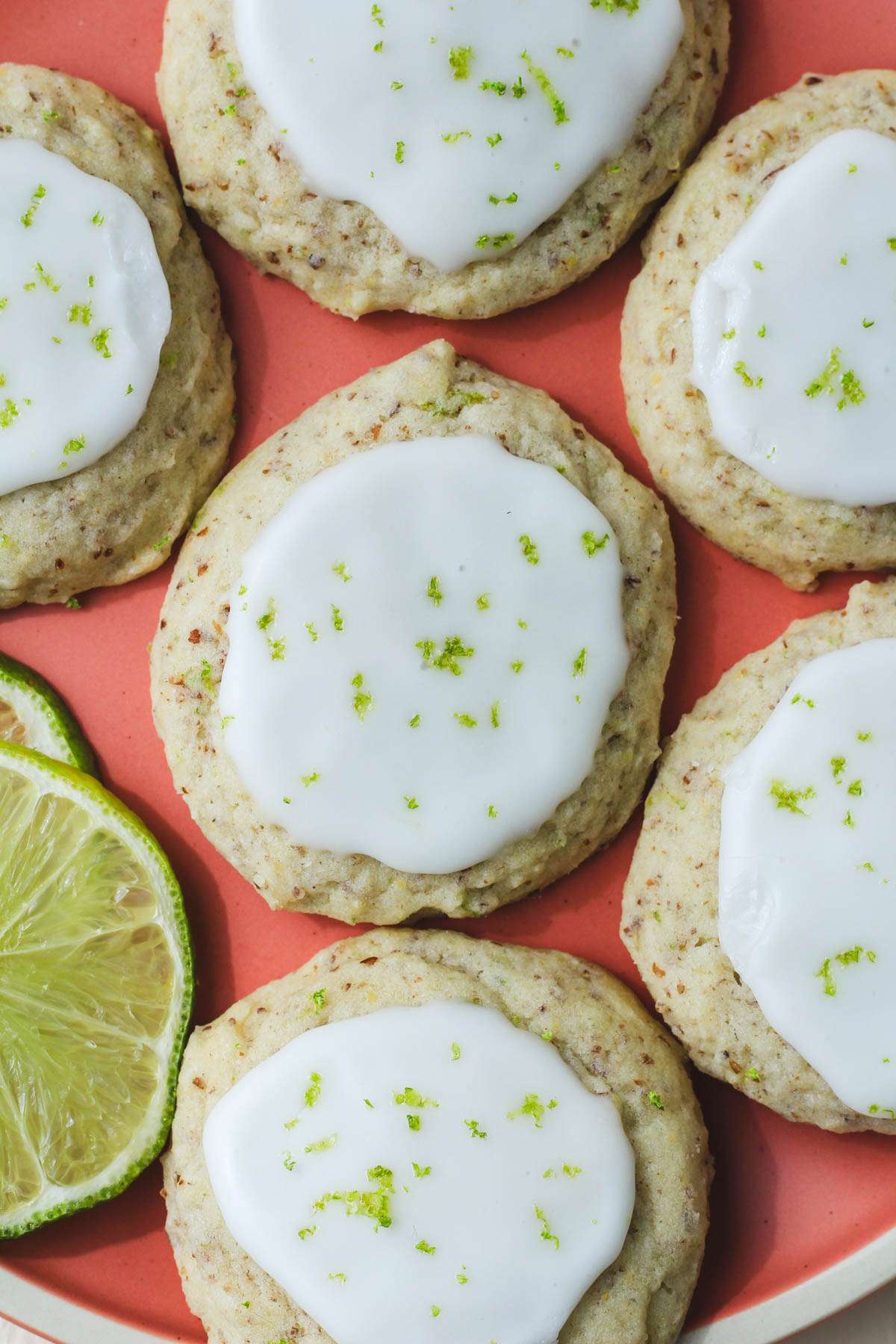 A pink plate with soft vegan lime cookies topped with lime glaze and lime zest.