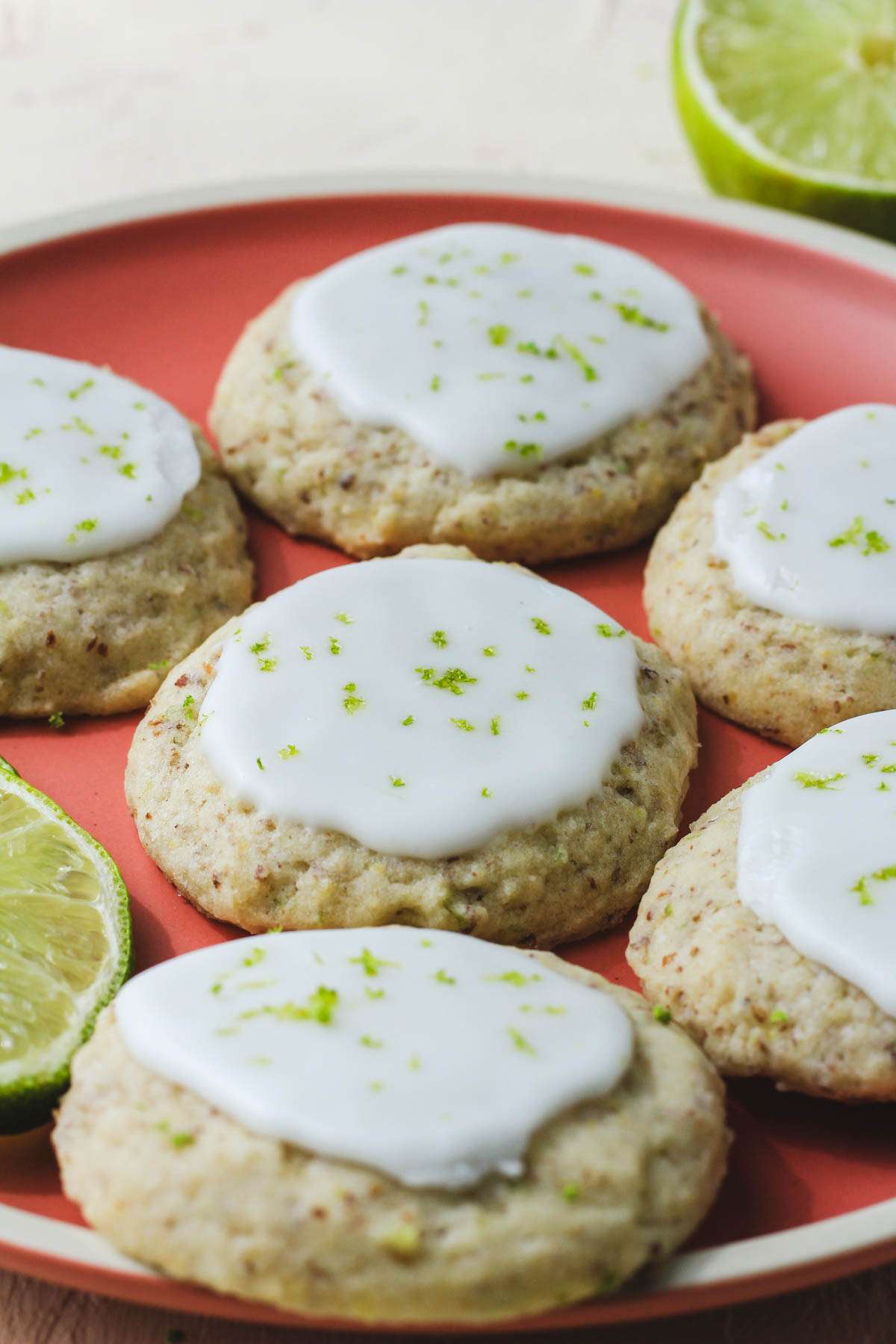 A pink plate with soft vegan lime cookies topped with lime glaze and zest.