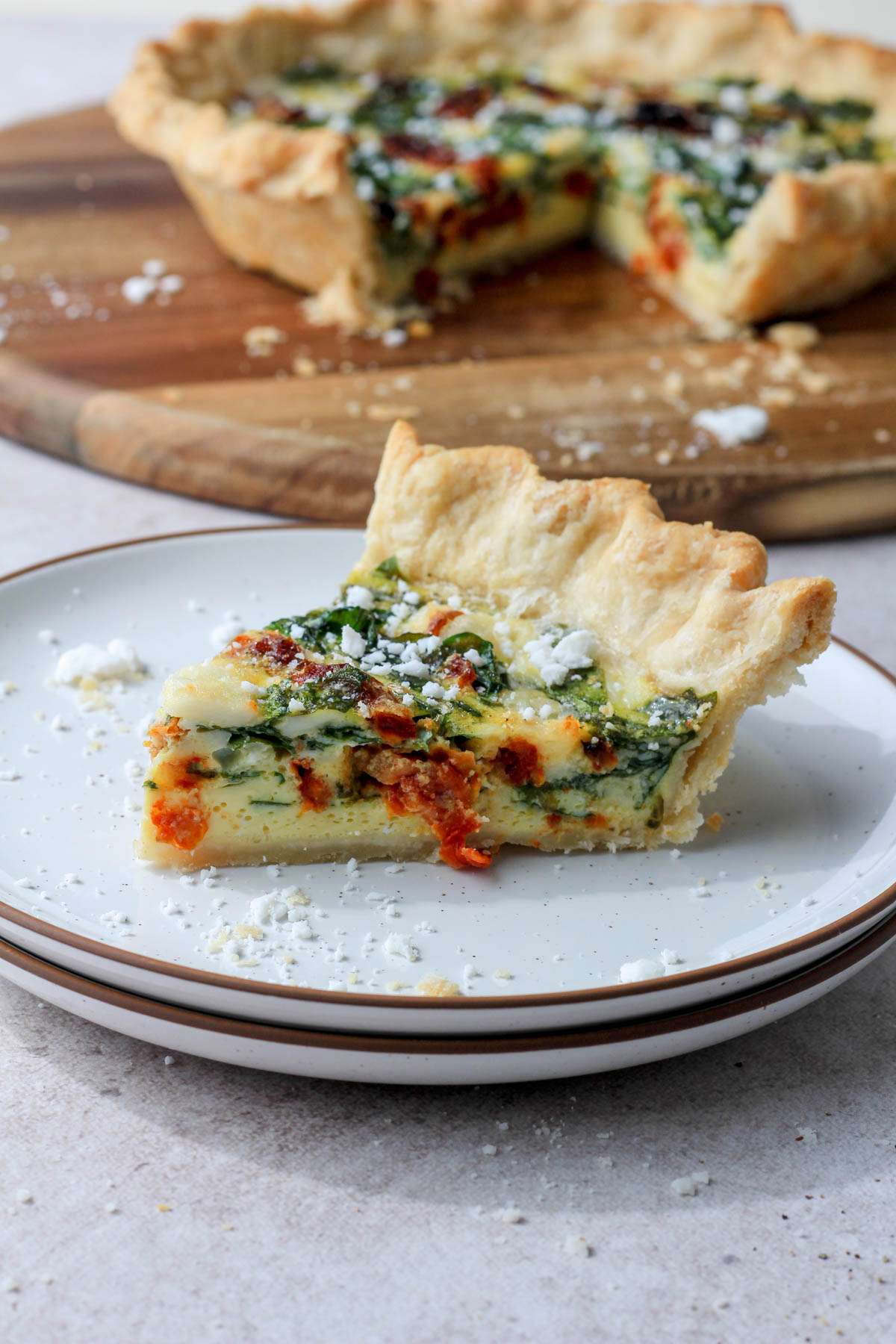 A stack of white plates with a brown rim topped with a slice of spinach, feta, and sun dried tomato quiche.