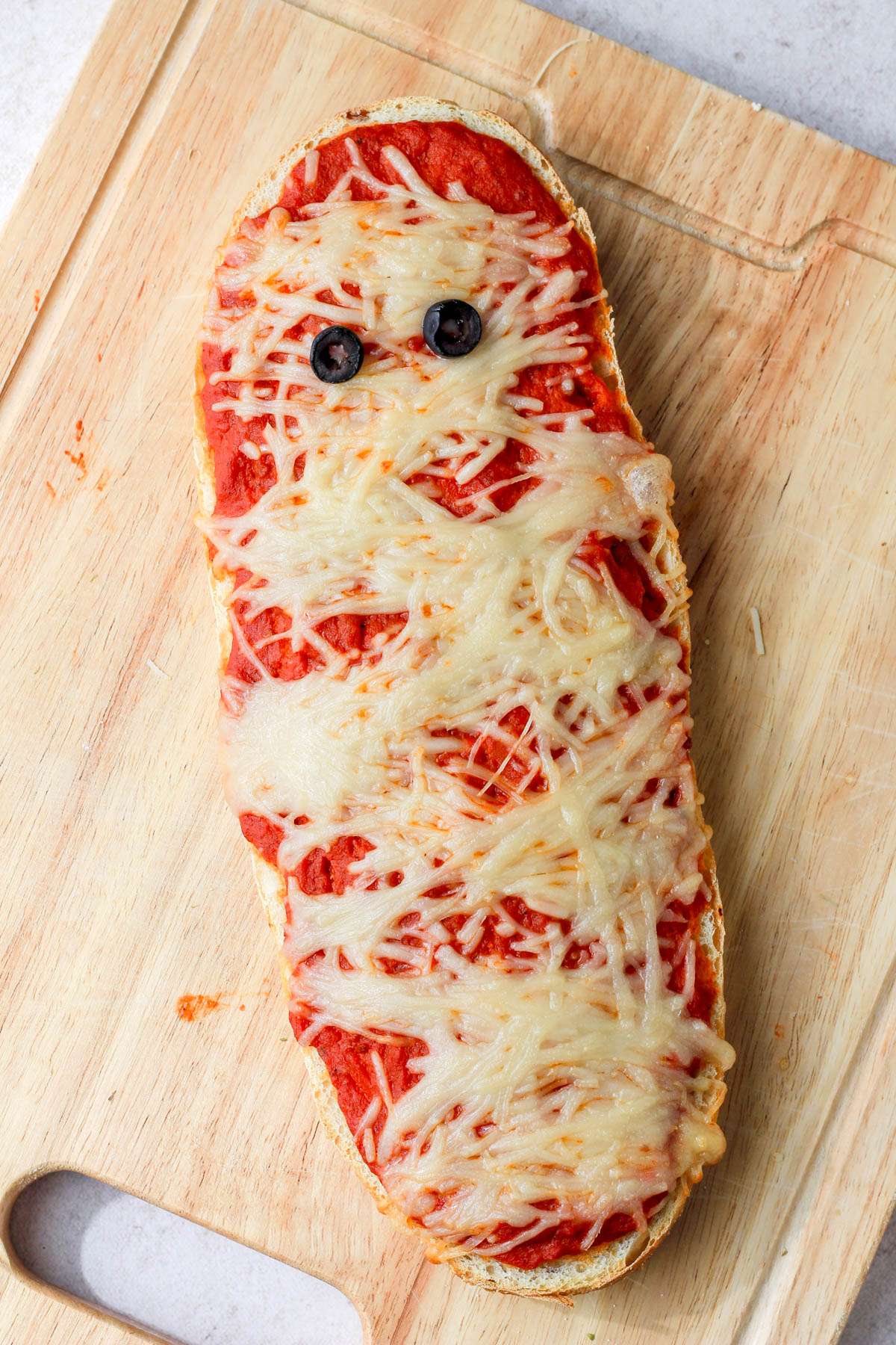 A wooden cutting board with a baked vegan mummy pizza.