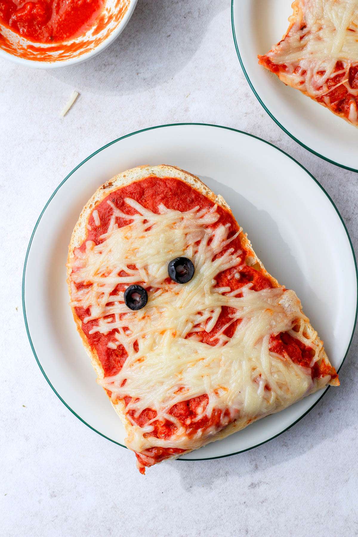 Vegan mummy french bread pizza head on a white and green plate.
