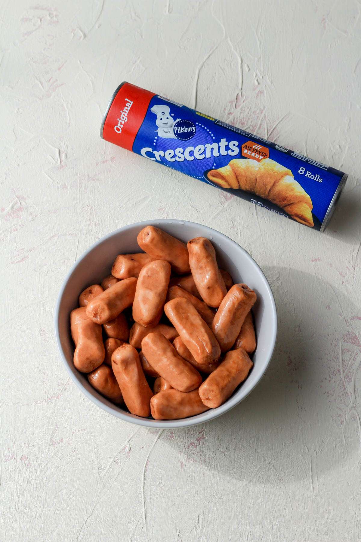 Ingredients for air fryer pigs in a blanket on a cream and pink counter.
