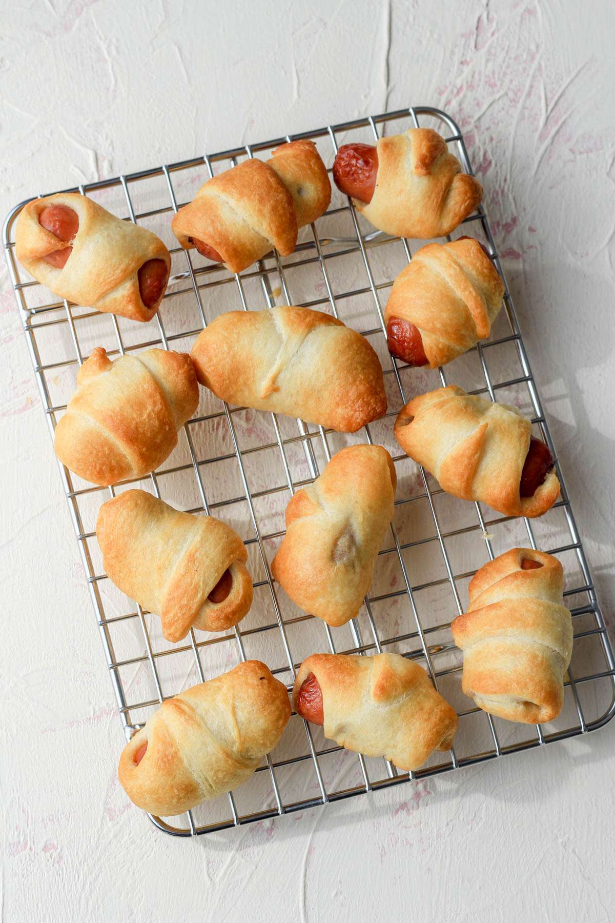 A small silver cooling rack with a dozen cooked pigs in a blanket.