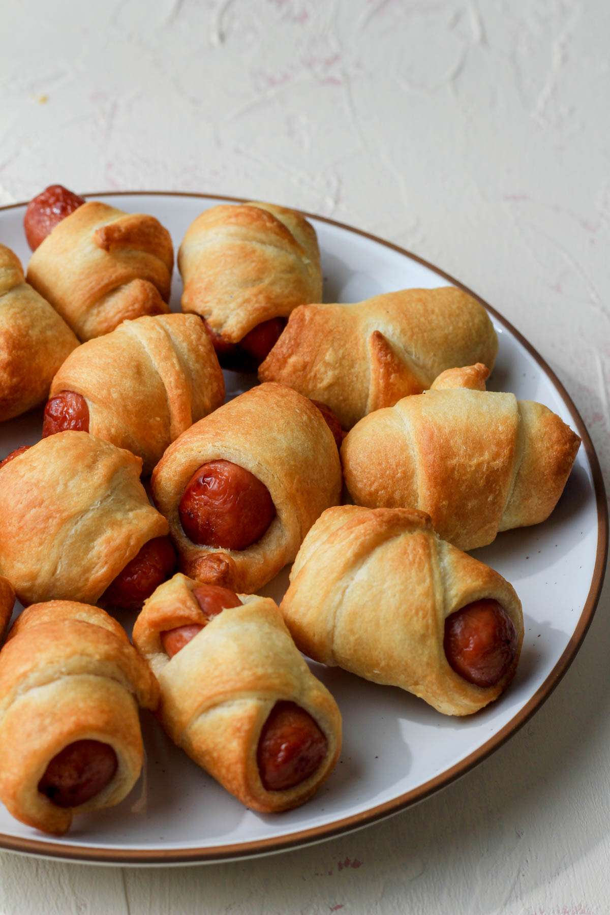 A white plate with a brown rim topped with air fryer pigs in a blanket.
