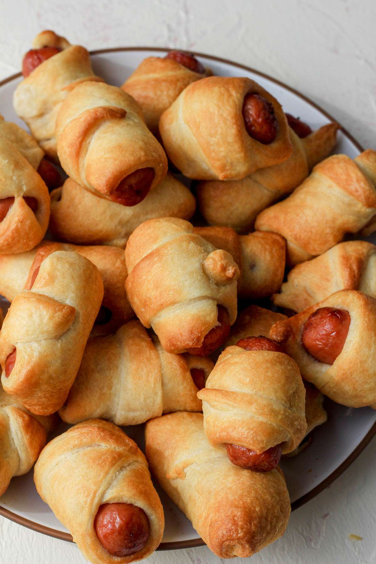 A top down picture of a white plate piled up with air fryer pigs in a blanket.