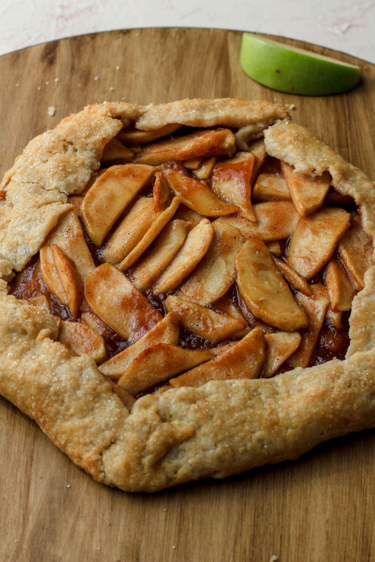 An apple galette on a wooden counter with a slice of apple in the back.