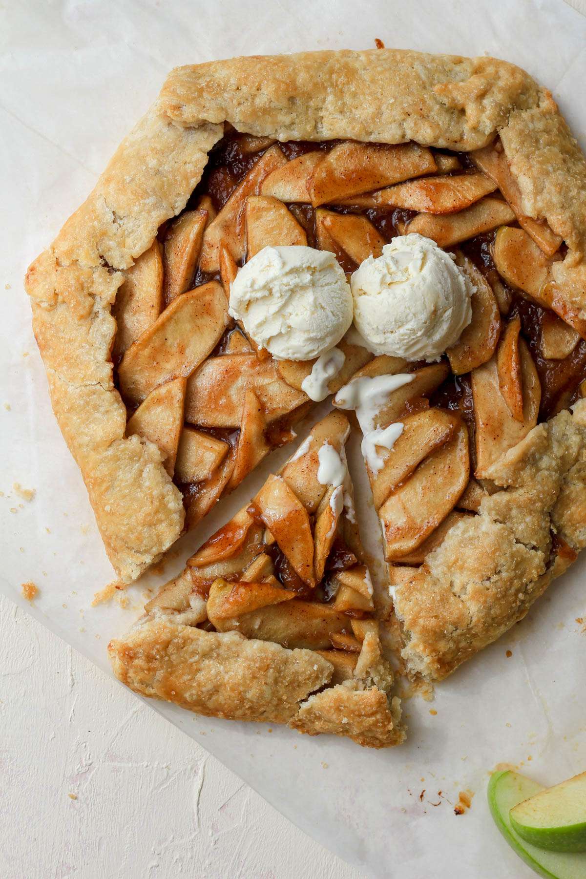A top down image of a dairy-free apple galette with a slice pulled out to the left and scoops of ice cream on top.