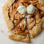 A slice of apple galette pulled a little to the left with two scoops of vanilla ice cream on top of the galette.