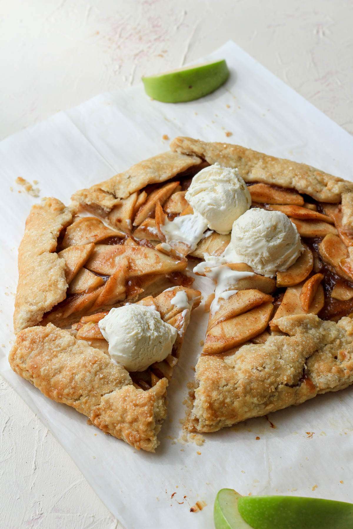 A parchment paper with an apple galette cut into two slices with scoops of vanilla ice cream on top.