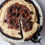 A close up of vegan no bake peanut butter oreo pie with a pie server lifting a slice out of the pan.