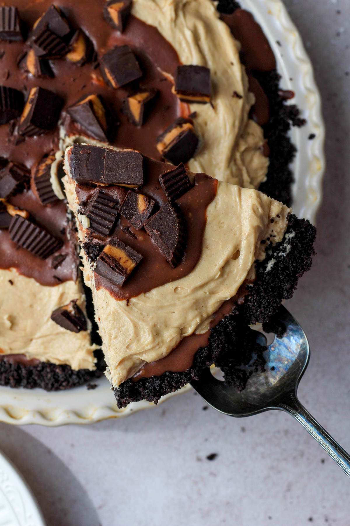 A fresh slice of vegan no bake peanut butter pie on a pie server hovering over the pie pan.