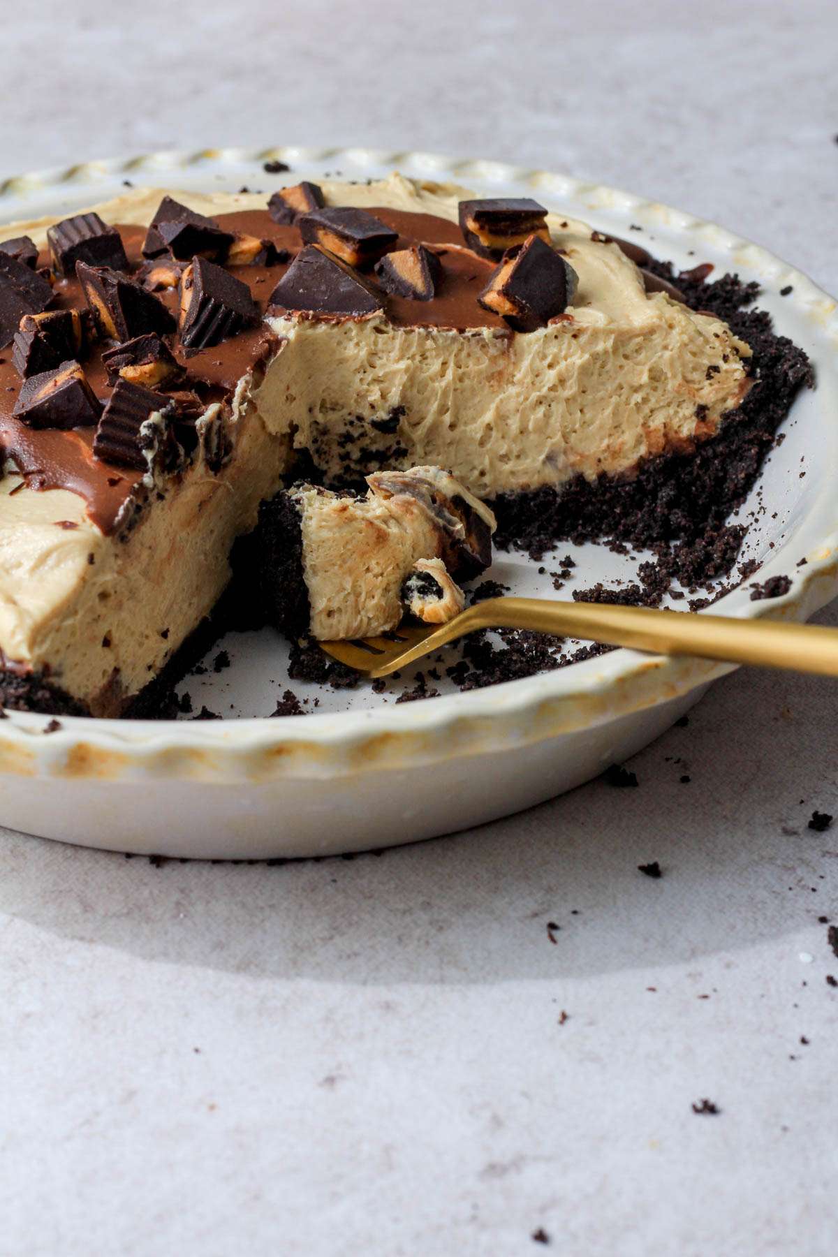 A golden fork with a bite of no bake vegan peanut butter Oreo pie in the pie pan with the rest of the peanut butter pie.