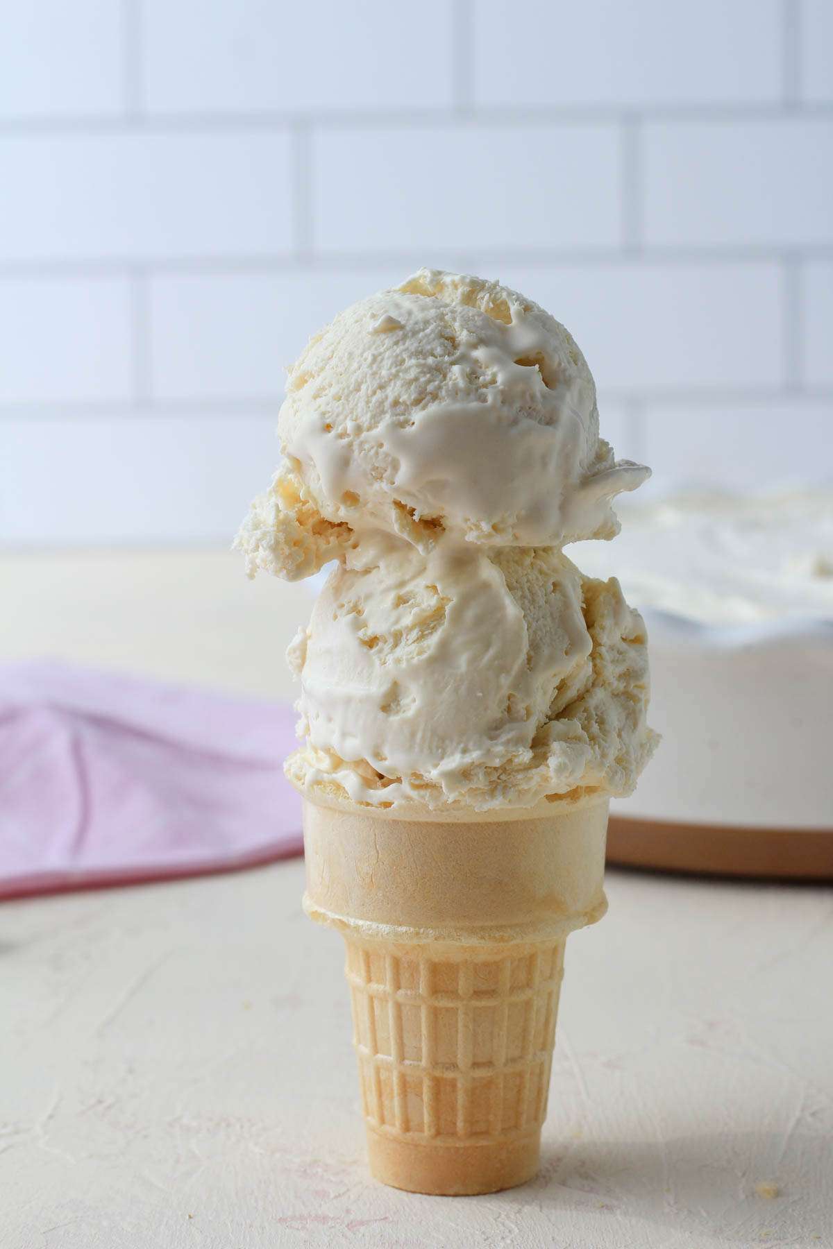 A cake cone topped with two scoops of no churn vegan vanilla ice cream on a cream counter with a white background.