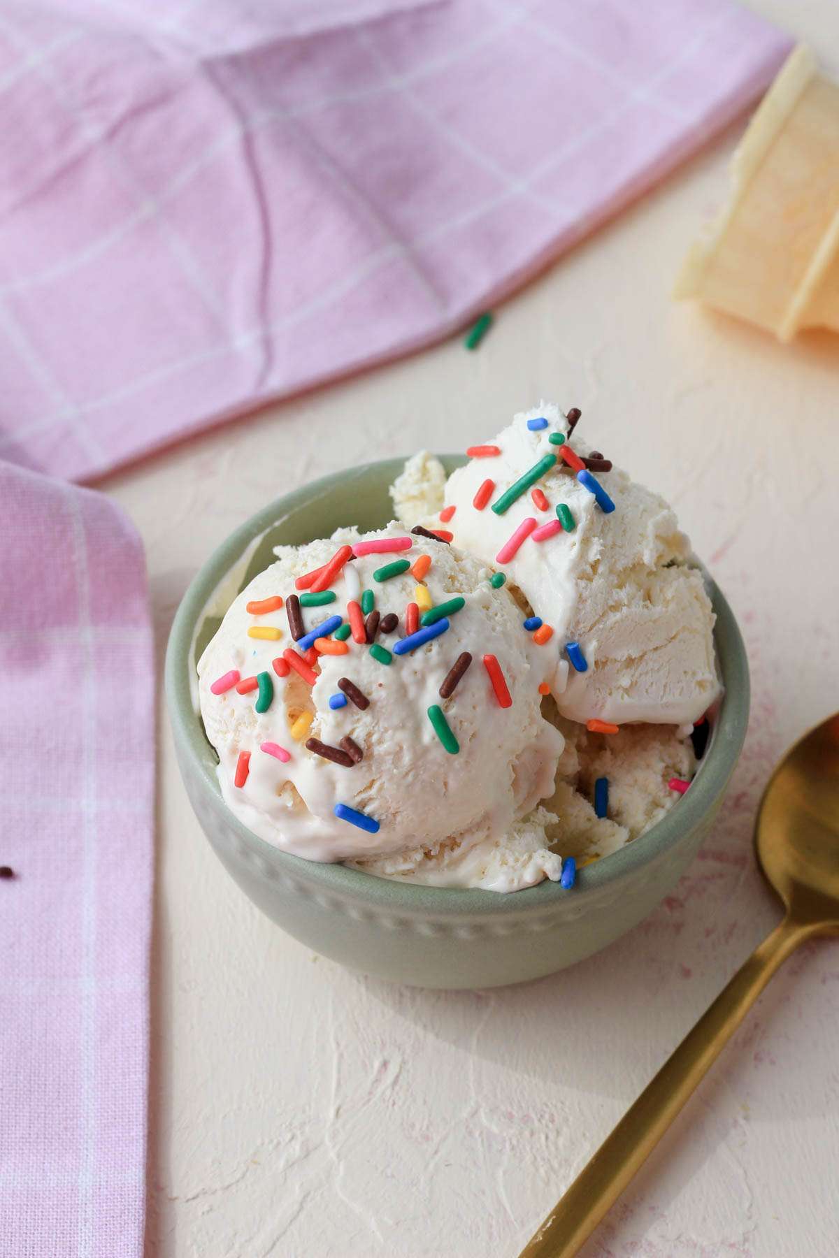 A small green bowl with scoops of no churn vegan vanilla ice cream topped with rainbow sprinkles.