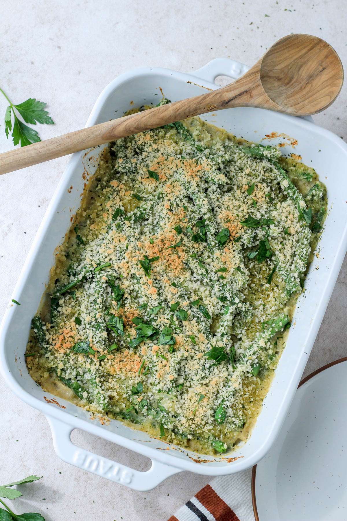A wooden spoon on top of a white baking dish with vegan green bean casserole made from scratch.