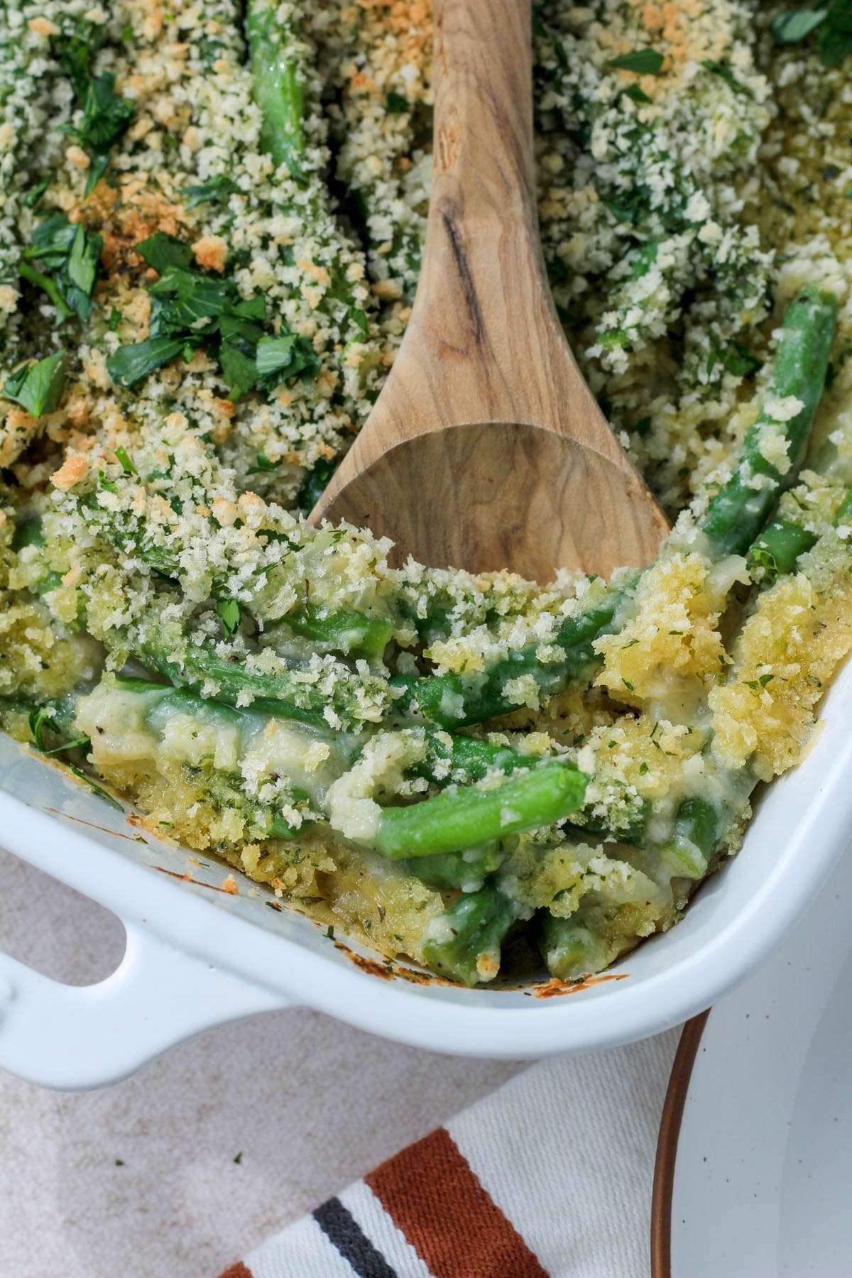A wooden spoon scooping out vegan green bean casserole from a white dish.