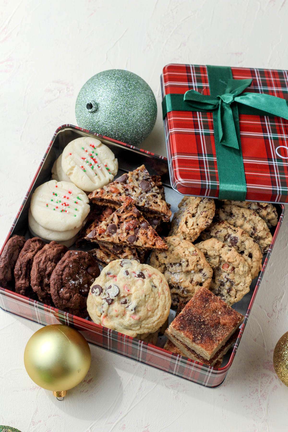 A green and red cookie box with the lid taken off and Christmas cookies inside.